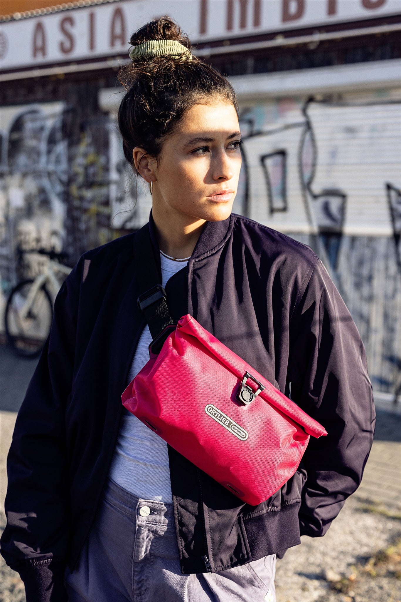 Ritratto di donna con borsa a tracolla ORTLIEB Velo-Sling Flex color cyber-pink in ambiente urbano.