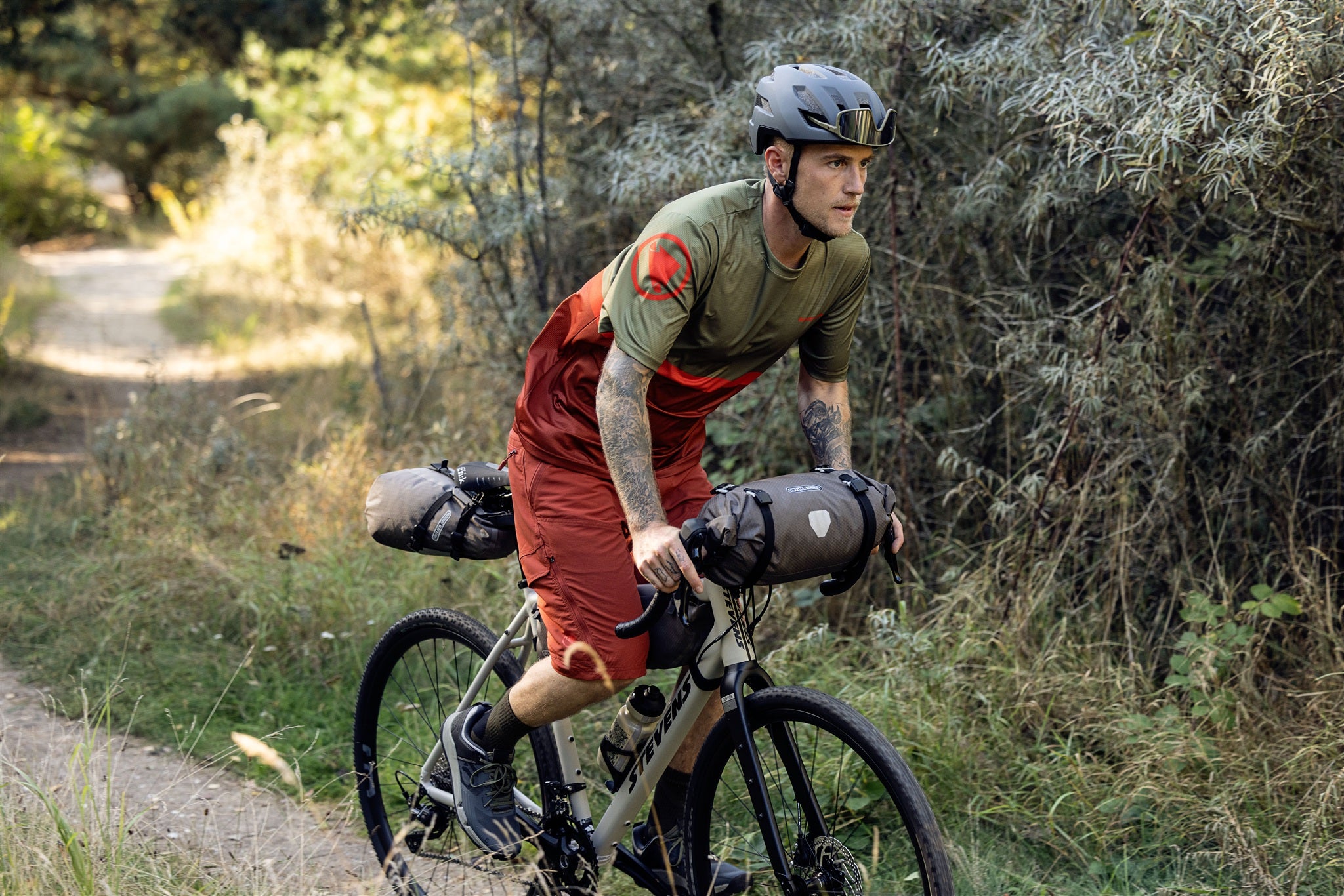 Ciclista ajusta la bolsa de manillar ORTLIEB Handlebar-Pack Flex color dark-sand en terreno irregular