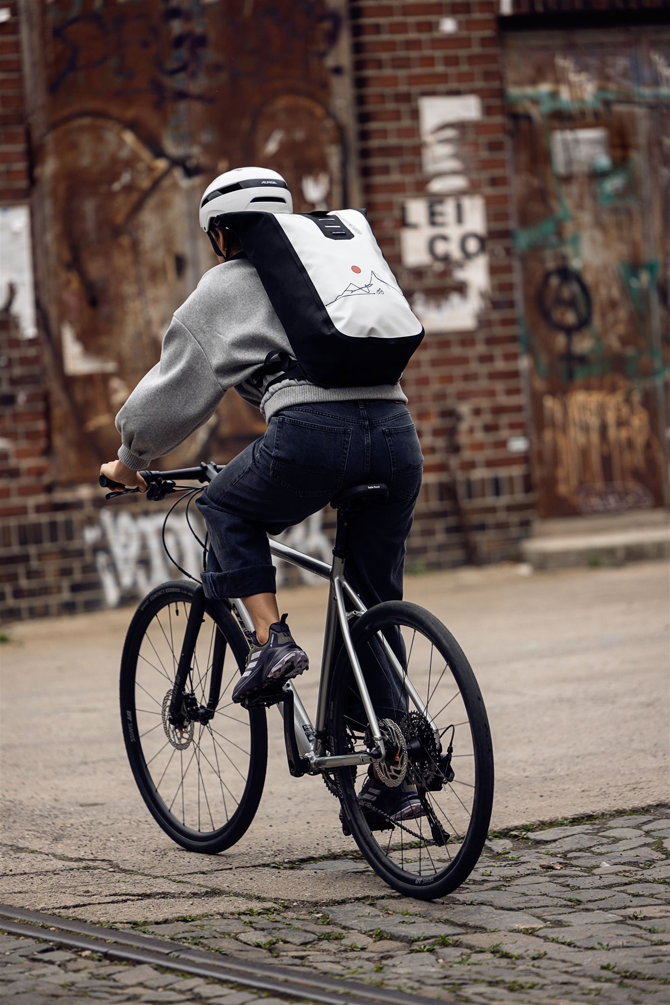 Mujer sentada en escalera metálica con mochila ORTLIEB Velocity Design blanca y negra con sol rojo