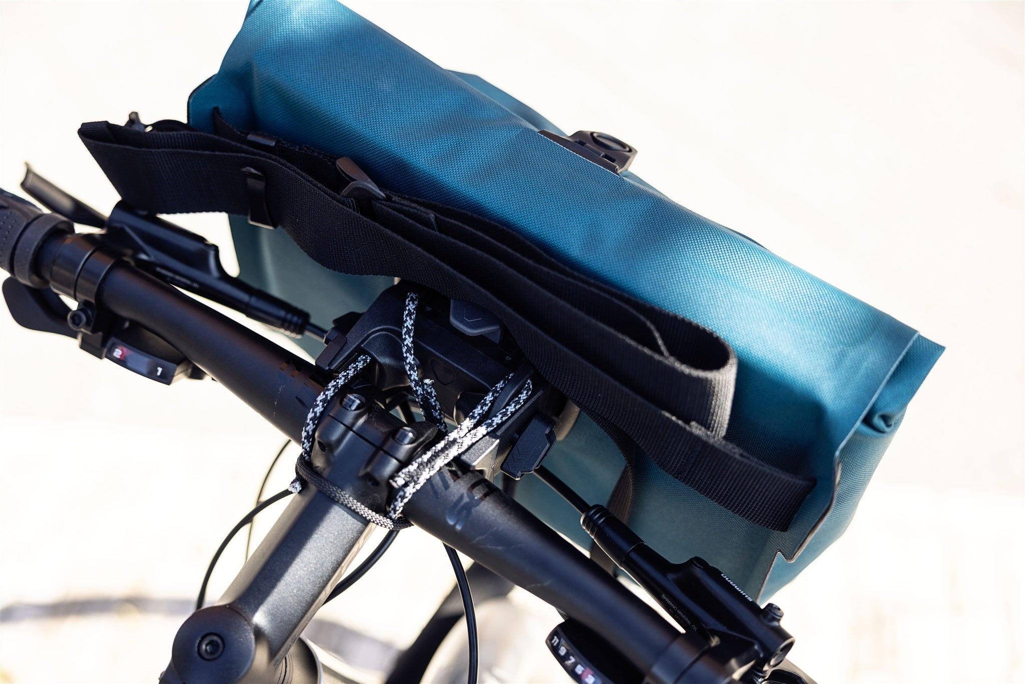 Primer plano de la bolsa de manillar ORTLIEB Velo-Sling Flex color petróleo con sujeción Bar-Lock de tejido impermeable en la bicicleta.